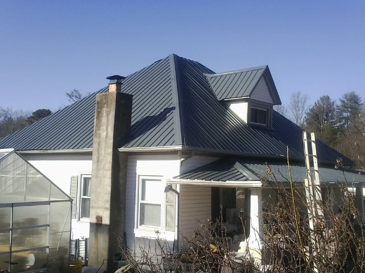 Dark blue standing seam metal roof on a white farmhouse with dormer — Slate & Tile Roof Repair by Roofing Brothers in Snover