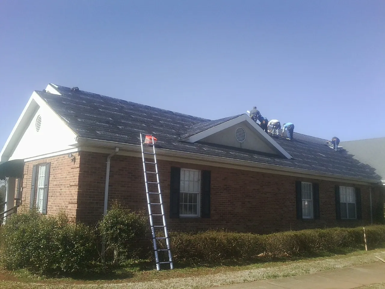 Crew tearing shingles off a brick ranch roof with a ladder set — Emergency Roof Repair work by our crew in Snover