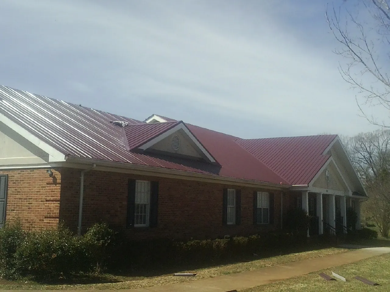 Red metal roof with gabled entries on a long brick building, from a Hail Damage Roof Repair job in Snover