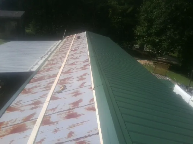 Old rusted panels beside newly installed green metal roofing — Wind Damage Roof Repair by Roofing Brothers in Snover