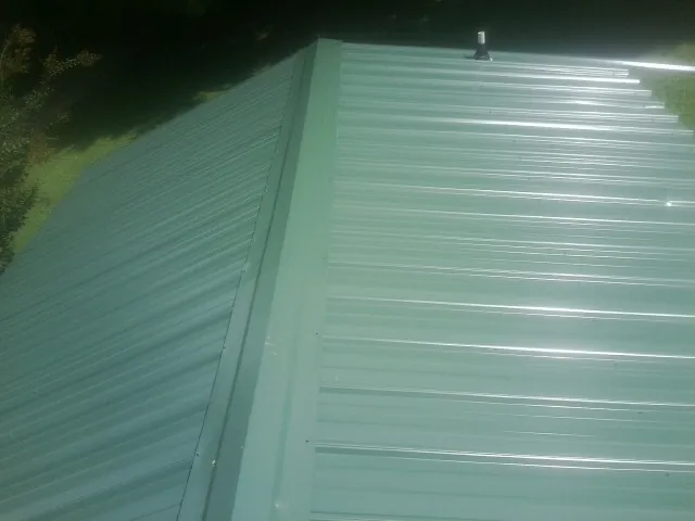 New green metal panels meeting at the ridge of a roof — Flat Roof Repair work by our crew in Snover