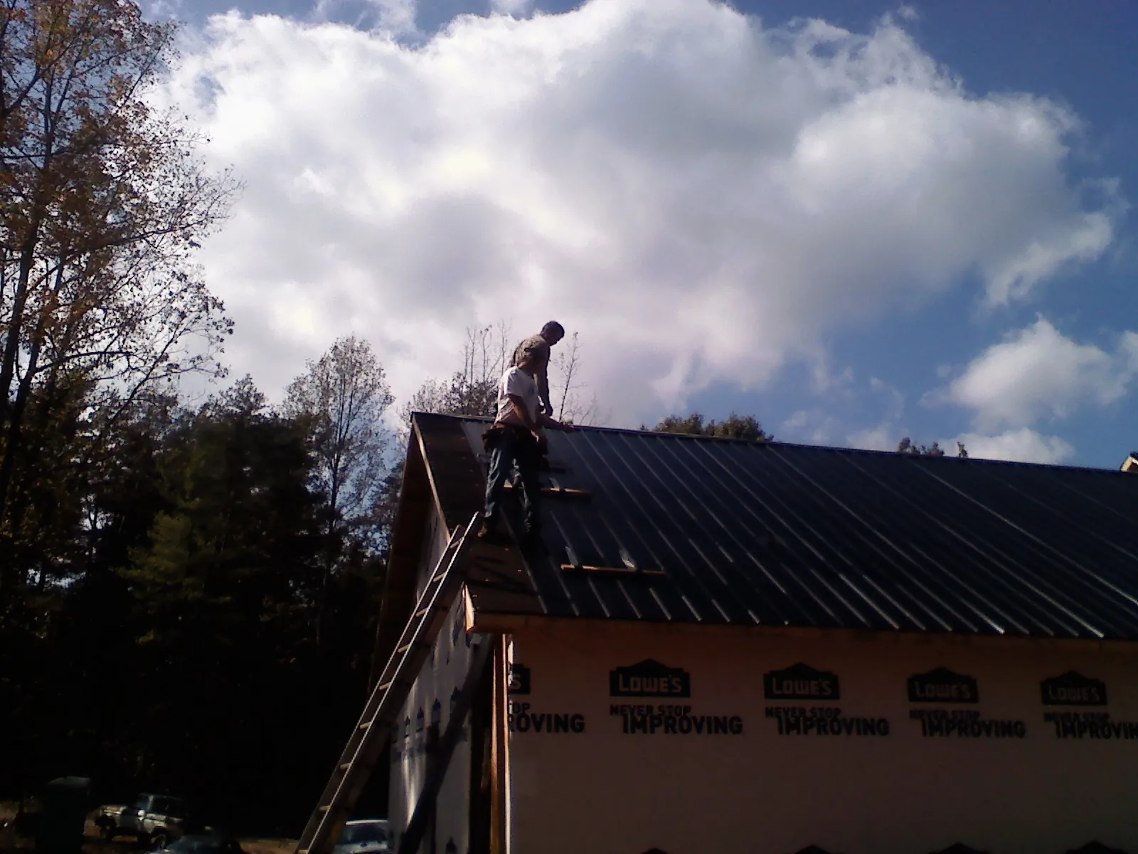 Roofer fastening dark metal panels high against a cloudy sky, from a Roof Inspection job in Snover