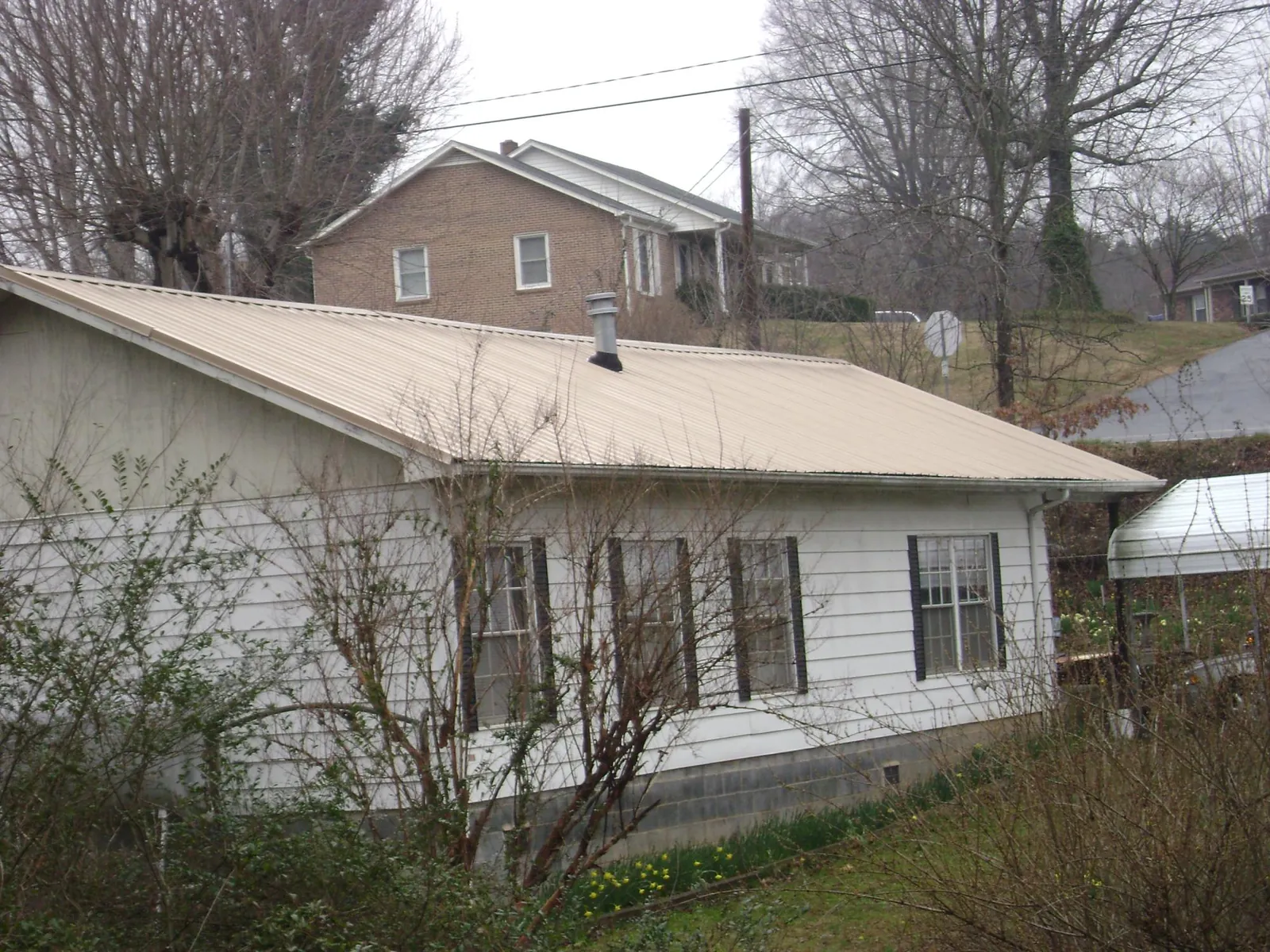 Tan metal roof on a white sided house set into a hillside — Commercial Roofing by Roofing Brothers in Snover