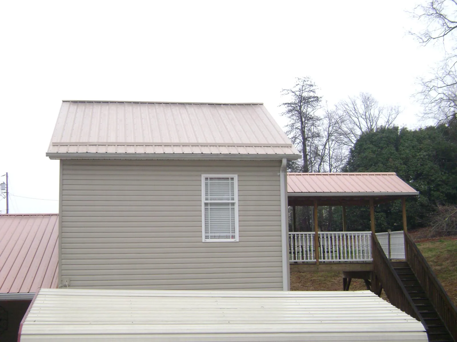 Tan metal roofs on a two story addition and attached porch, from a Roof Replacement job in Snover